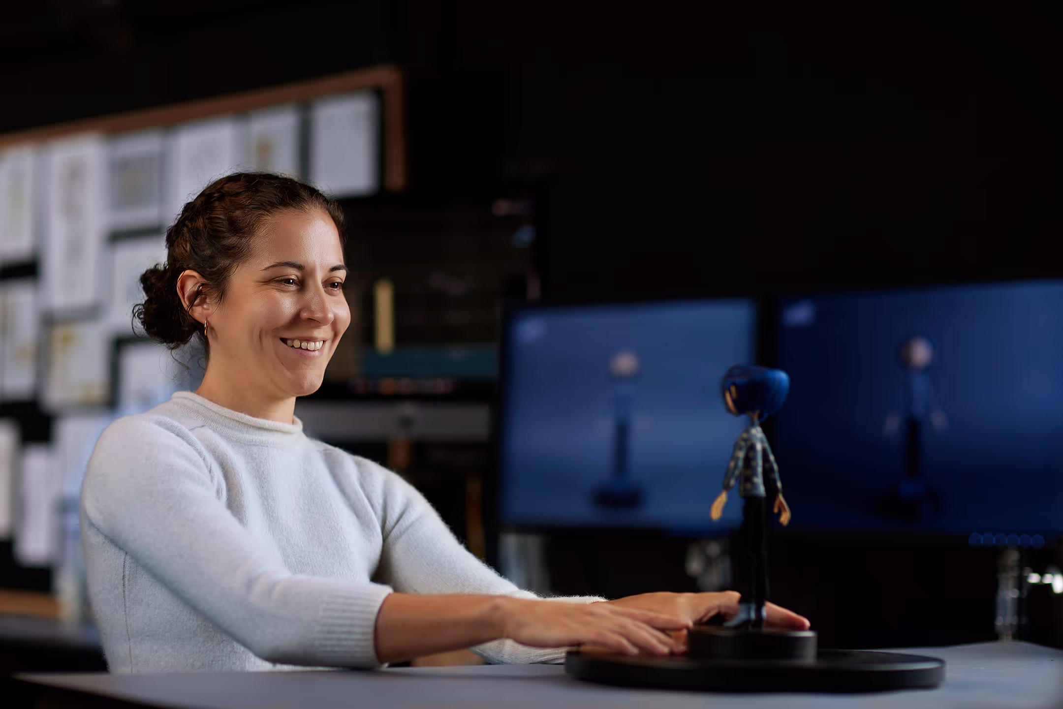 Woman sits at a desk admiring a Coraline puppet